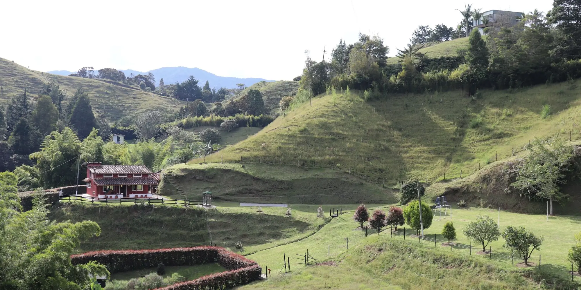 Una casa de campo en una ladera de potrero con bordes de bosque y potreros cercados en El Retiro, Antioquia, Colombia.